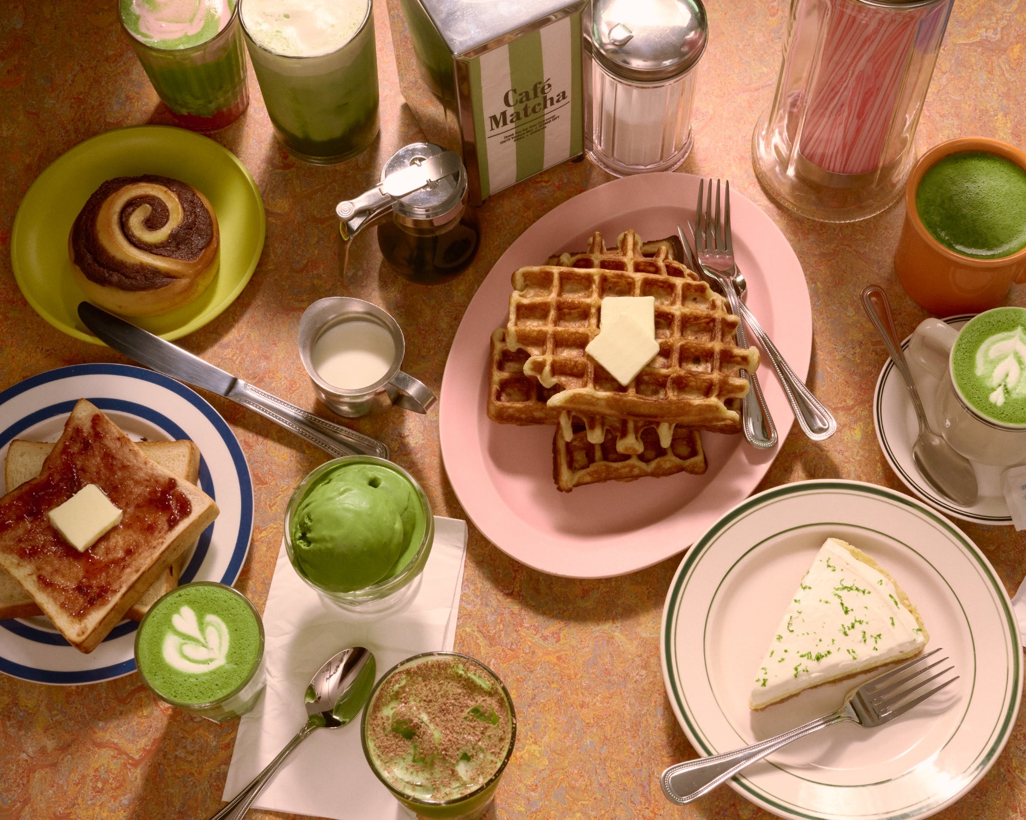 Breakfast table with waffles, toast, and green drinks on a wooden surface.